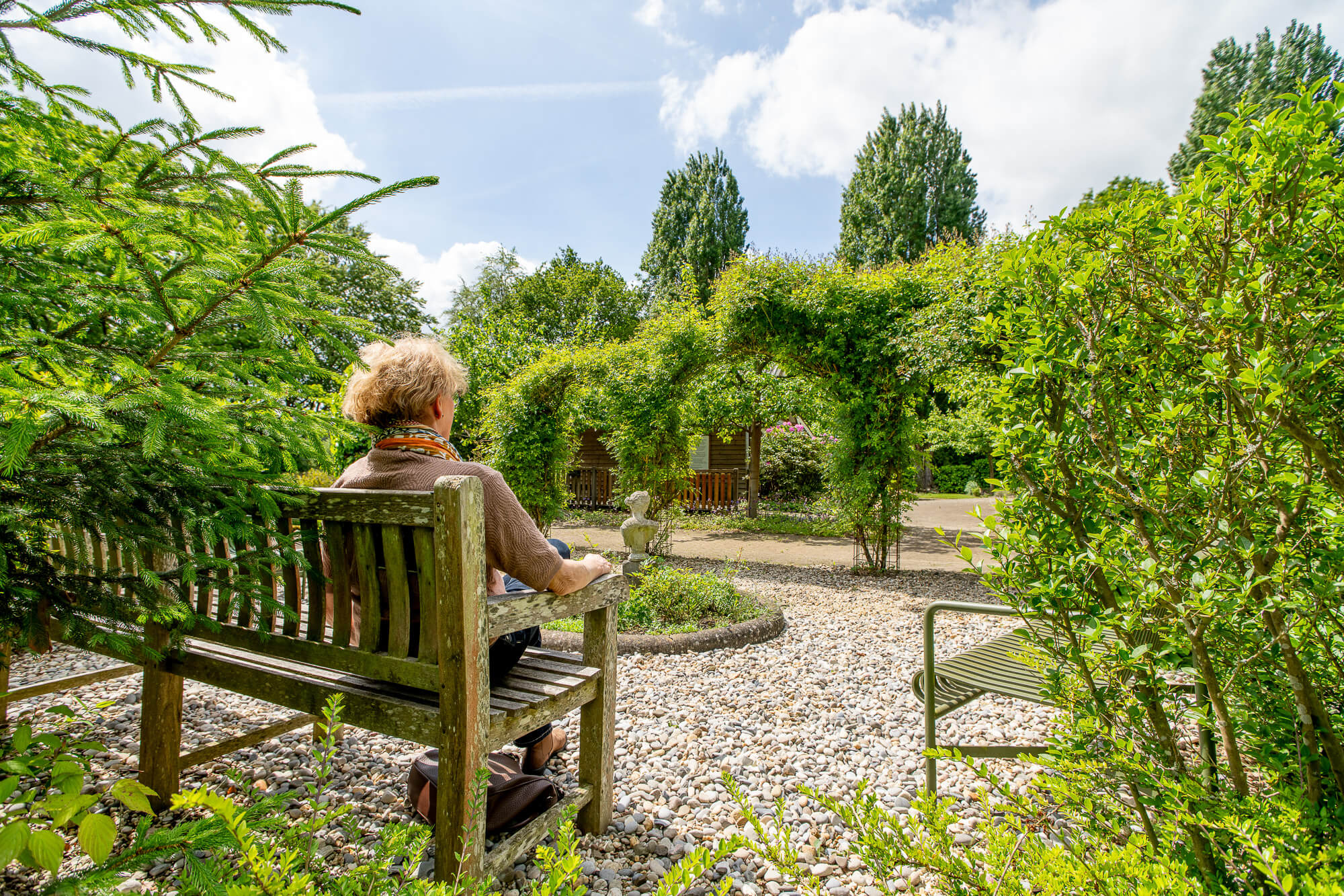 Oudere vrouw geniet op een bankje in een mooie rustige tuin